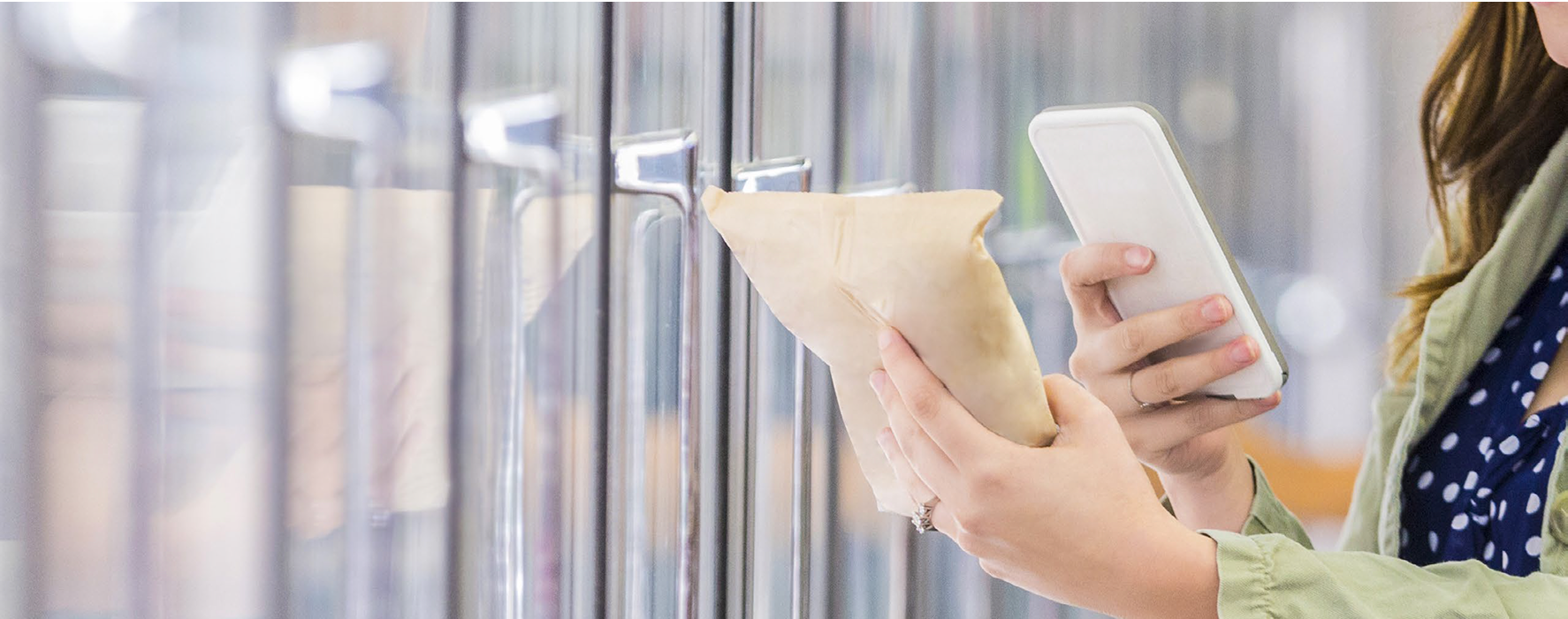 Woman standing in front of refrigerated grocery store shelves, holding a packaged item in one hand and a smartphone in the other, scanning the product to check information while shopping.