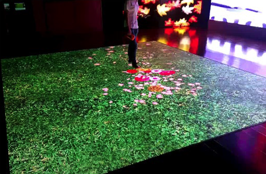 Person standing on an interactive digital floor display featuring animated grass and flowers that respond to movement